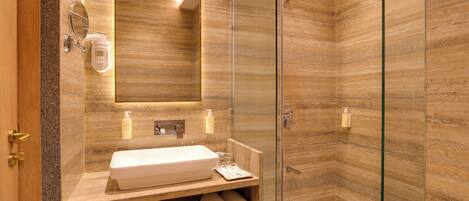 A modern bathroom with a glass shower enclosure, a wooden vanity with a white sink, and neatly rolled towels.