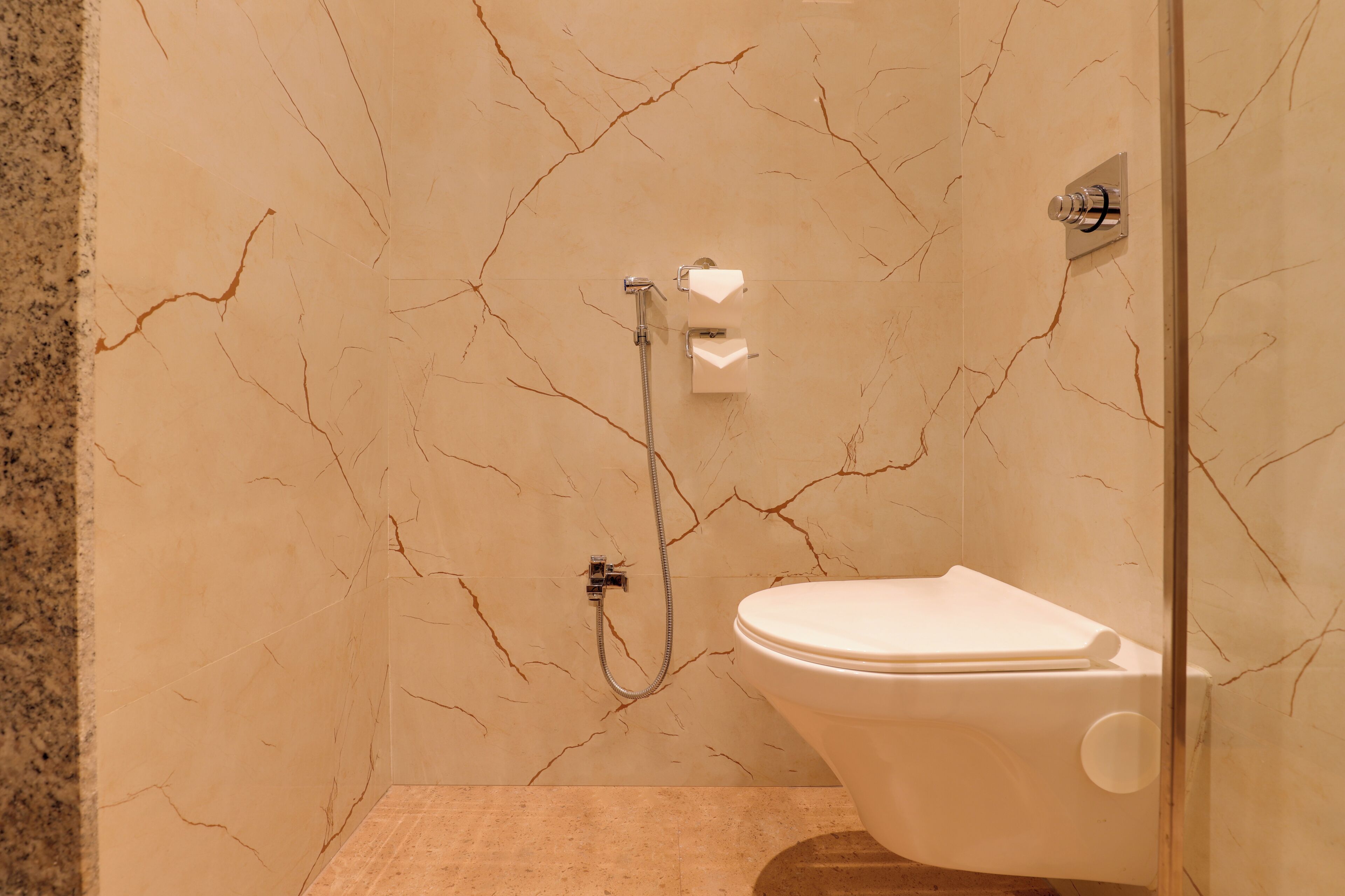 Un baño con pared de mármol, ducha y inodoro.