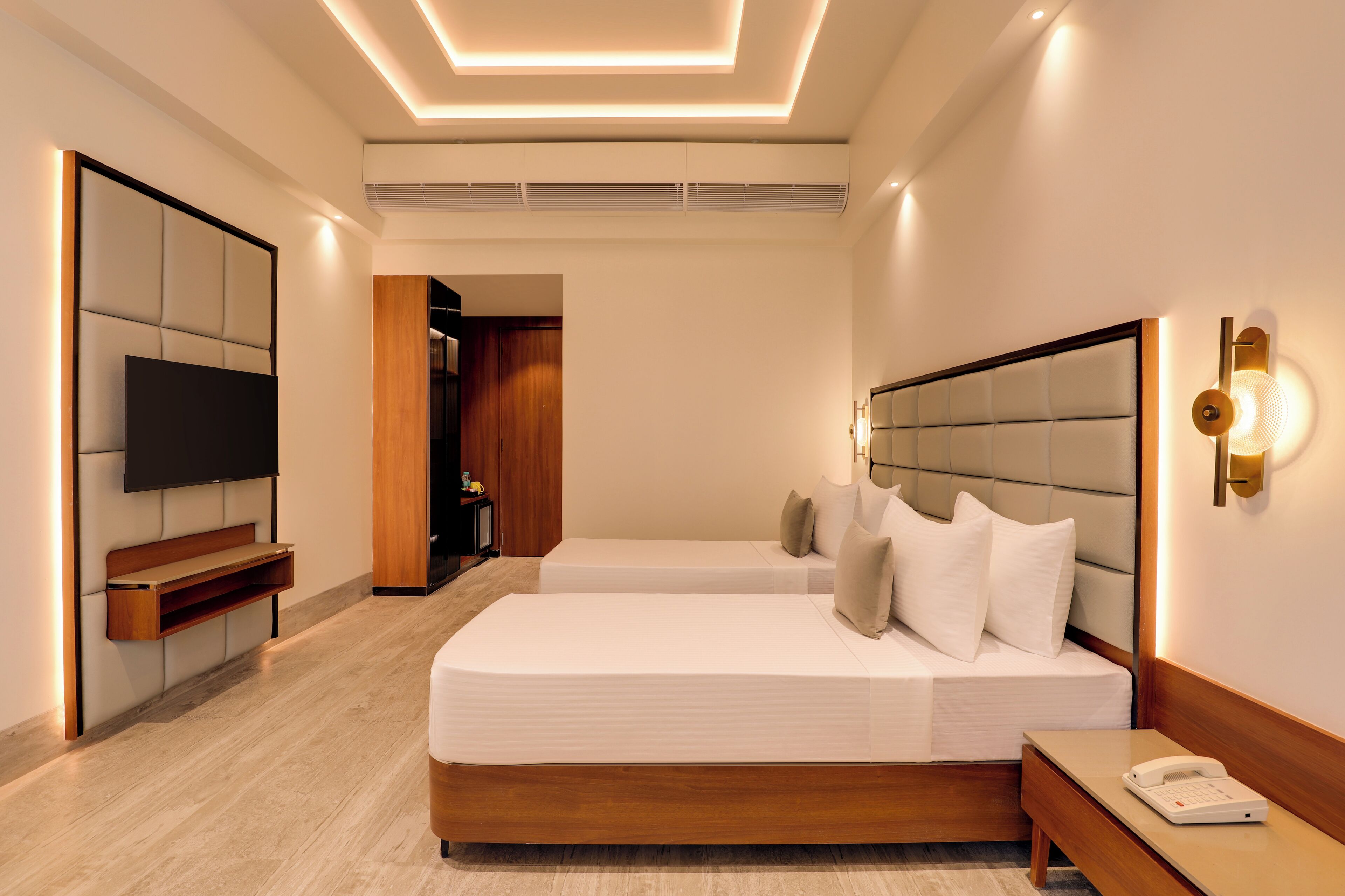 A modern hotel room with a large bed, bedside tables, a TV, and a wooden cabinet.