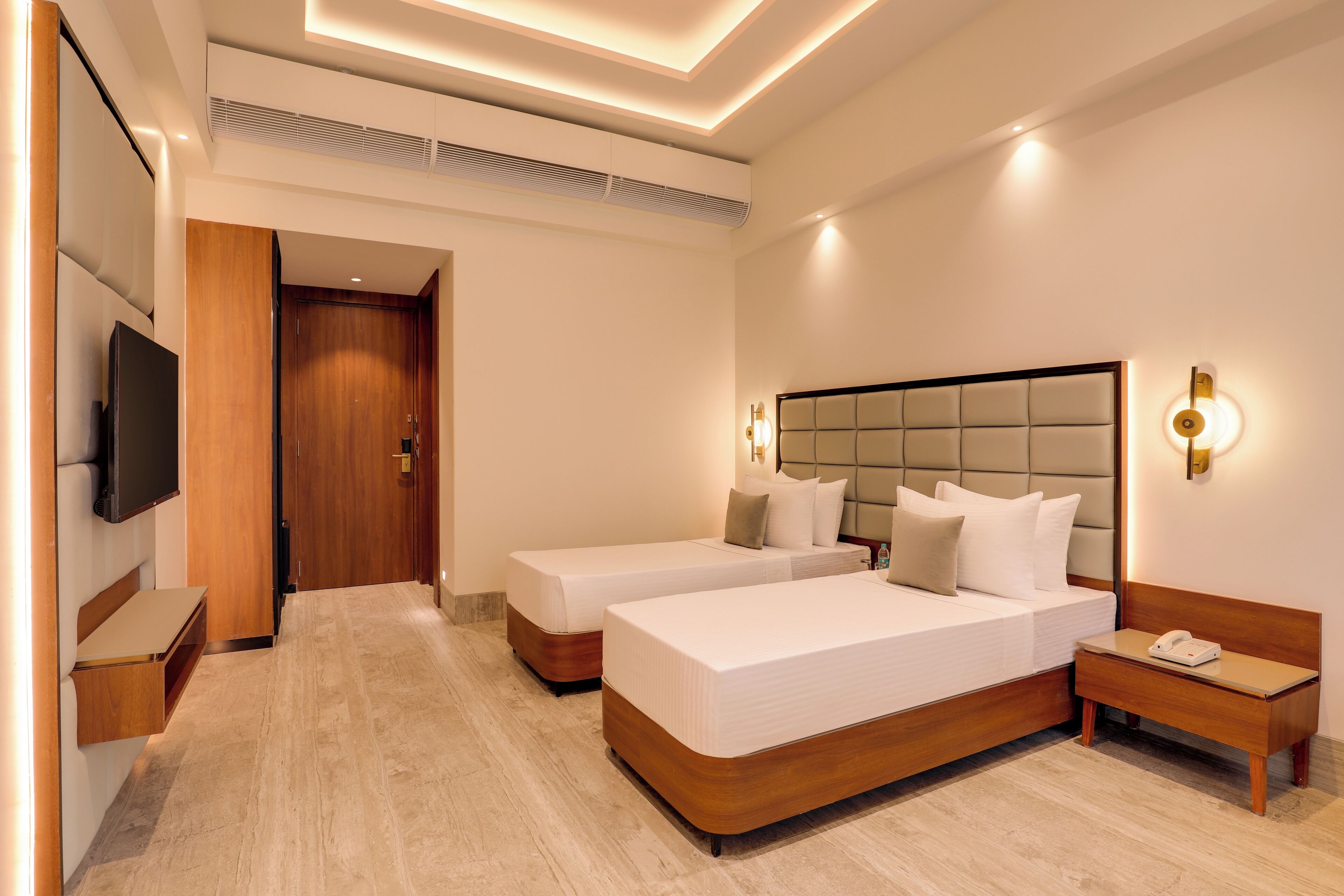 A hotel room with two beds, a TV, a bedside table, and a nightstand.