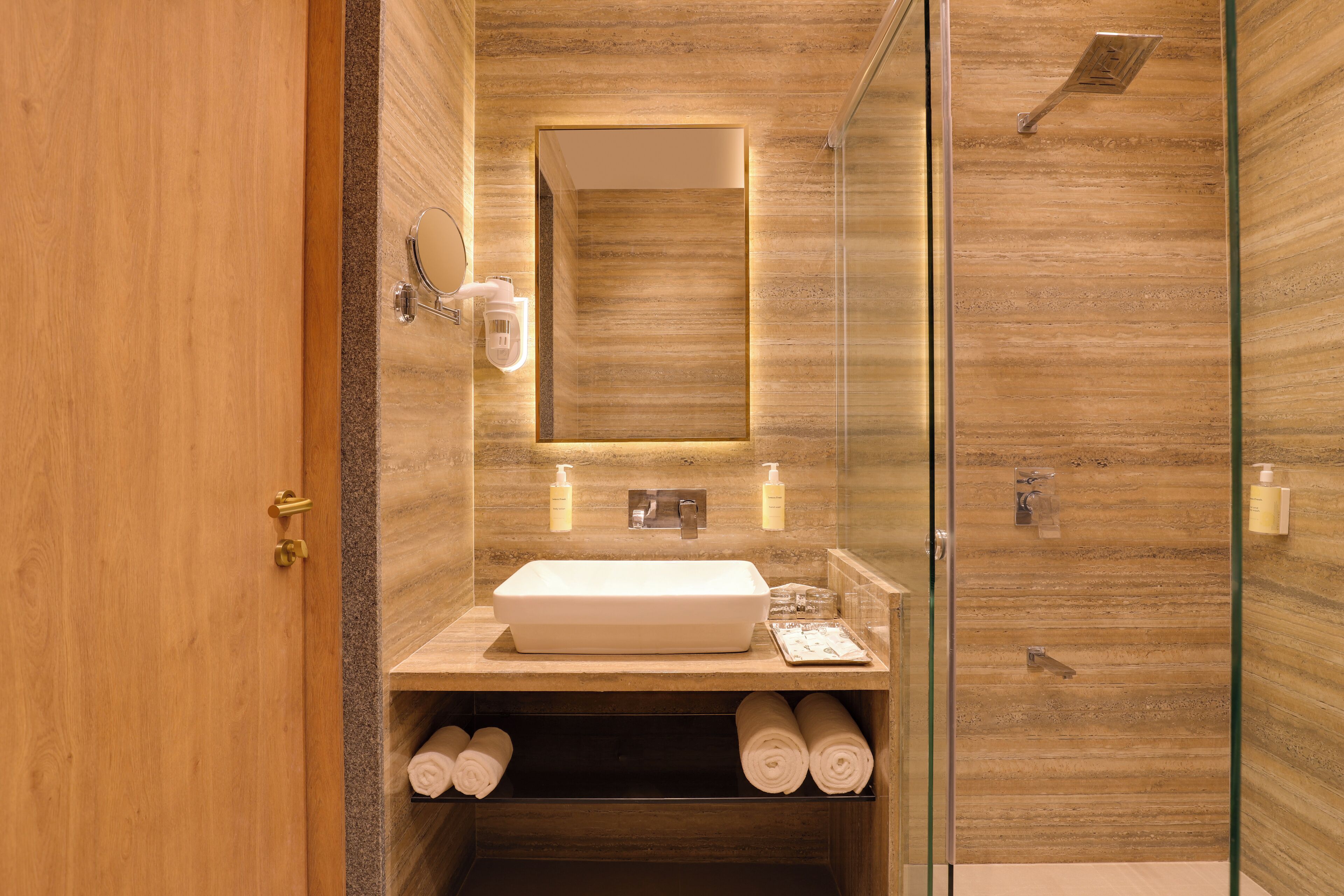 Un baño moderno con tocador de madera, cabina de ducha con mampara de vidrio y espejo integrado.