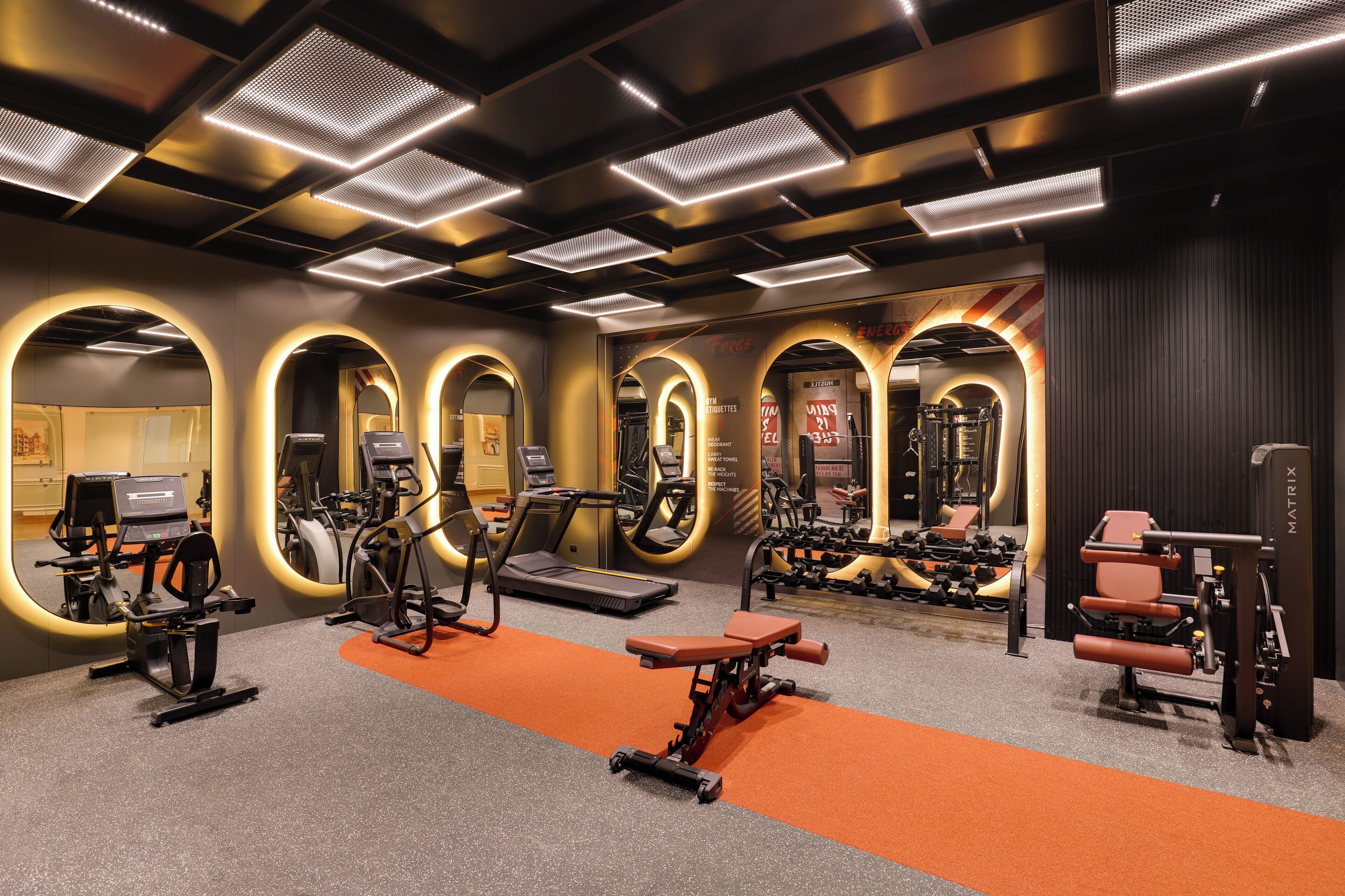 Un gimnasio moderno con diversos equipos de ejercicio, incluyendo cintas de correr y máquinas de pesas, dispuesto en un espacio amplio.