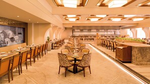 Uma sala de jantar ampla, com várias mesas e cadeiras, uma ilha central com balcão e um design de teto moderno com iluminação embutida.