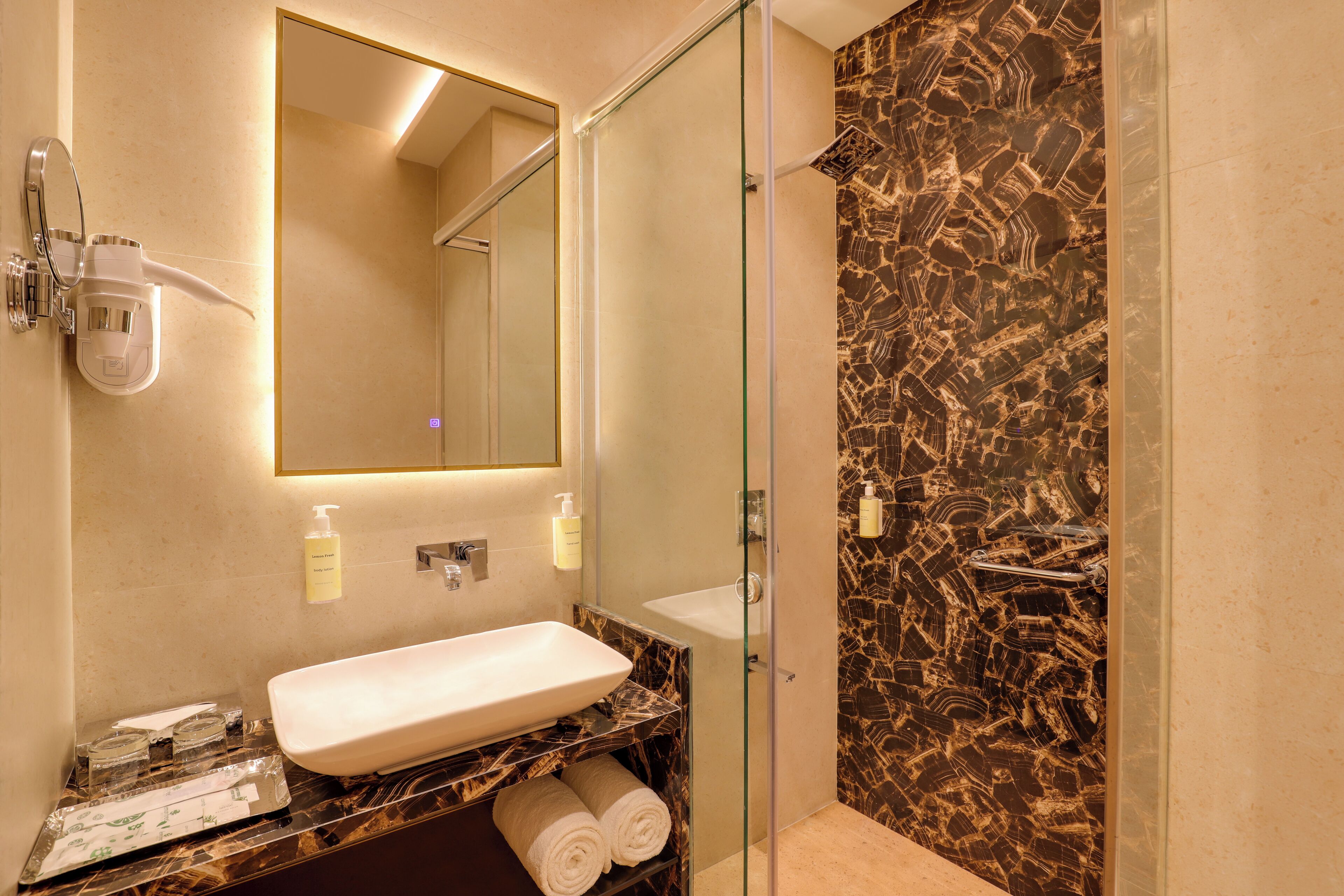 Une salle de bain avec un lavabo en marbre, une cabine de douche en verre et un miroir au-dessus du lavabo.