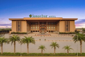 Stunning hotel exterior with a modern design, central entrance, and lush palm trees.