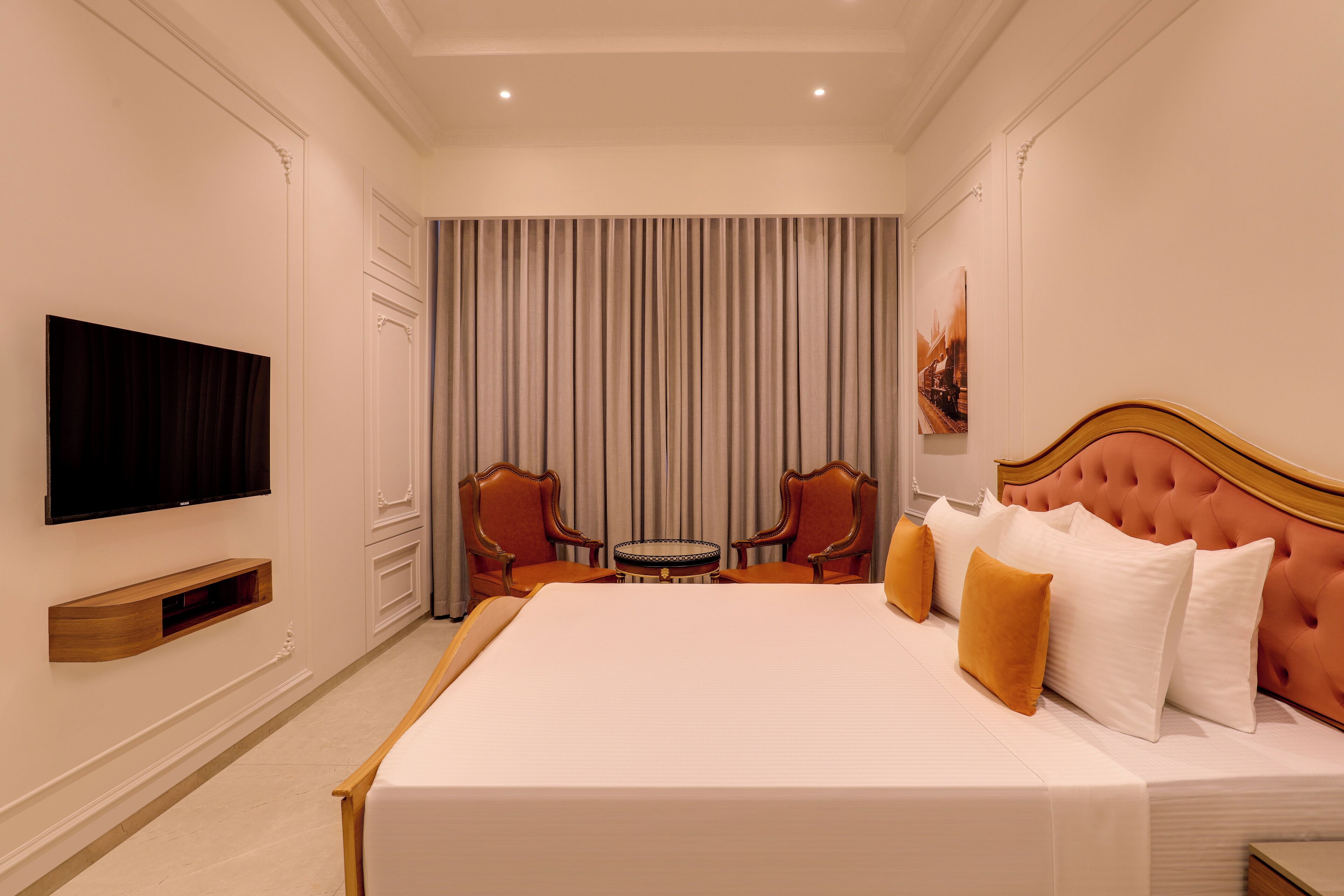 A hotel room with a large bed, a television mounted on the wall, a small round table, and two chairs.