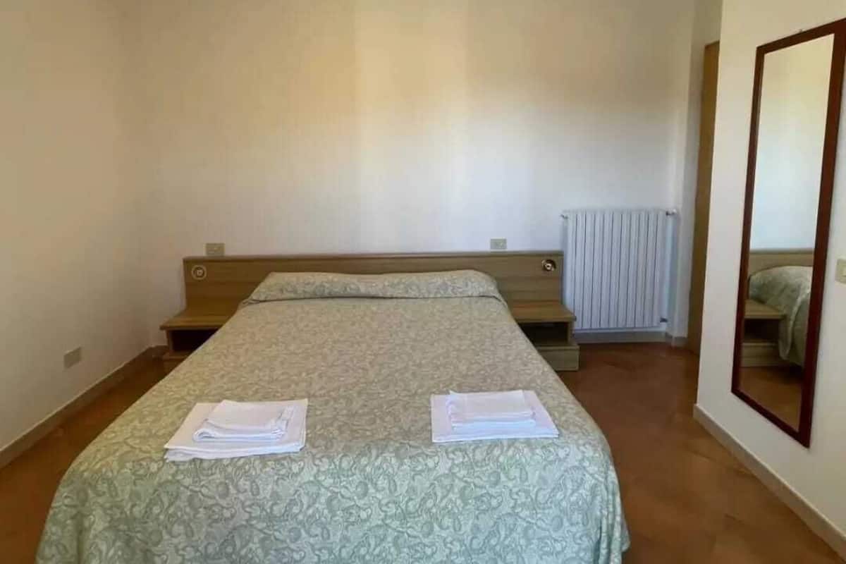 Habitación individual con una cama y colcha estampada, una mesita de noche, un espejo y un radiador.