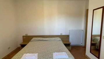 Une chambre avec un lit simple, une couvre-lit à motifs, une table de chevet, un miroir et un radiateur.