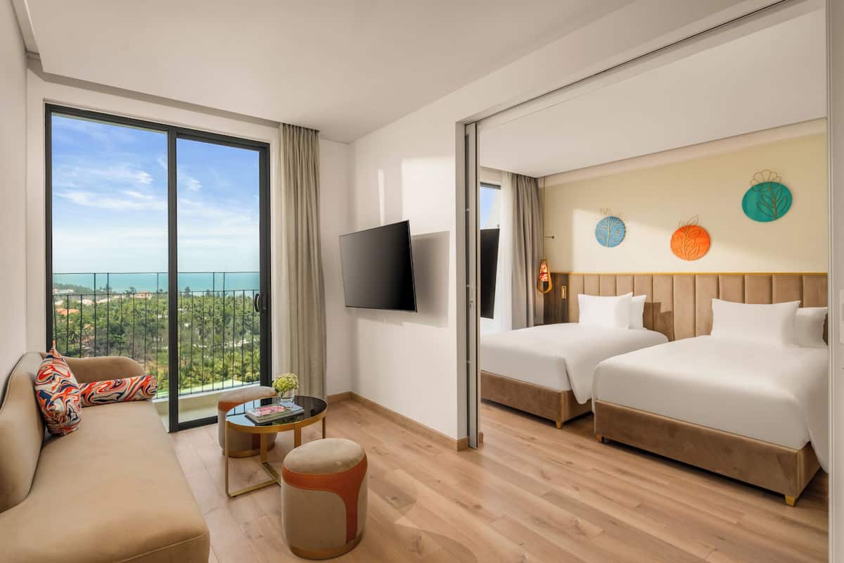 A hotel room with a balcony, a sofa, two beds, a TV, and a small table with a plant.
