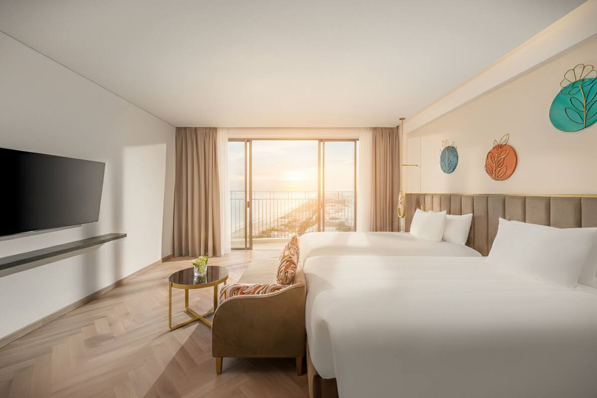 A hotel room with a large bed, a TV, a small table, and a view of the city.