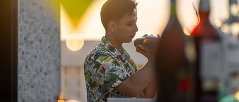 A person in a tropical shirt at a bar with bottles and a light fixture in the background.