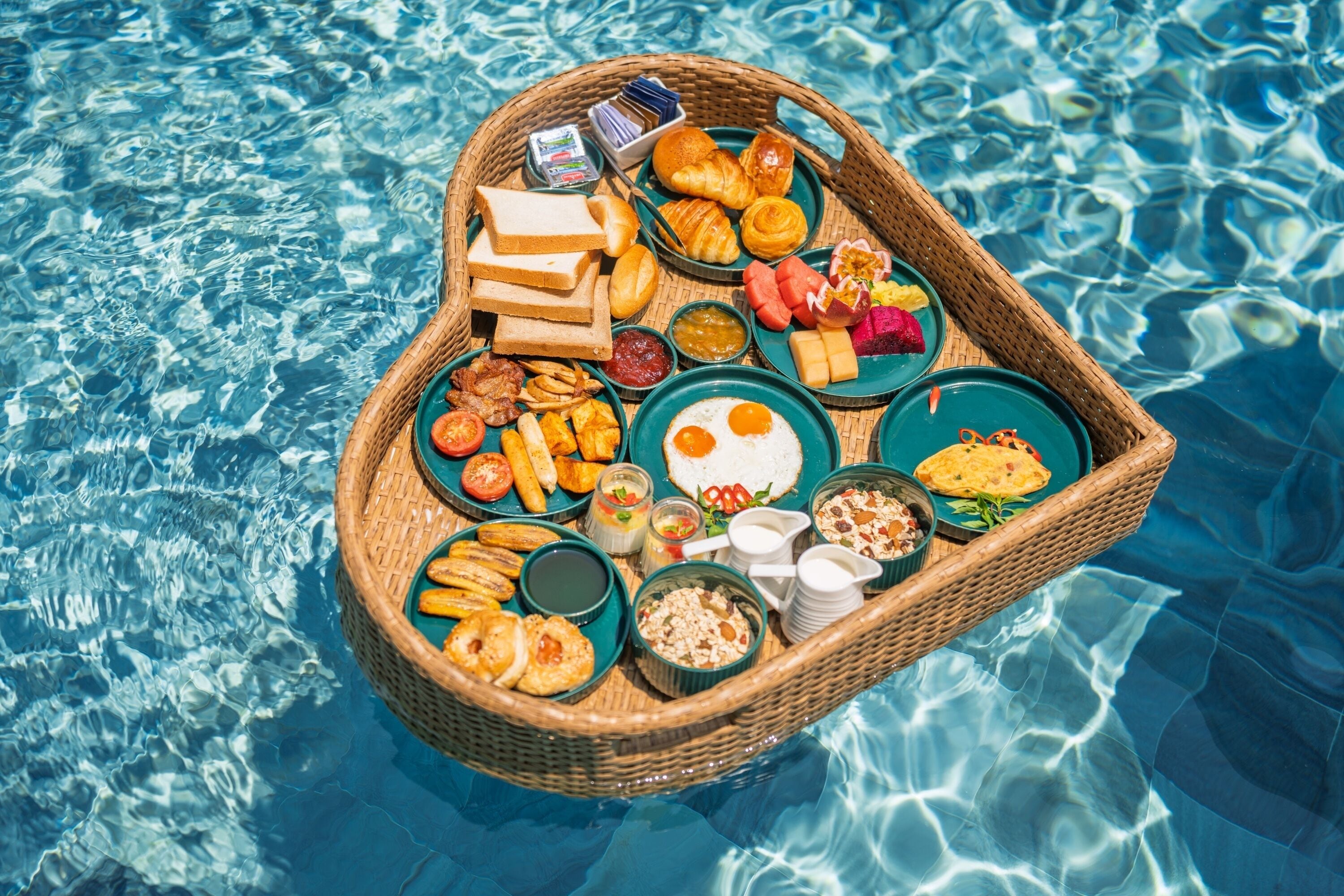 Un panier en forme de cœur rempli de produits pour le petit-déjeuner, flottant sur une piscine.