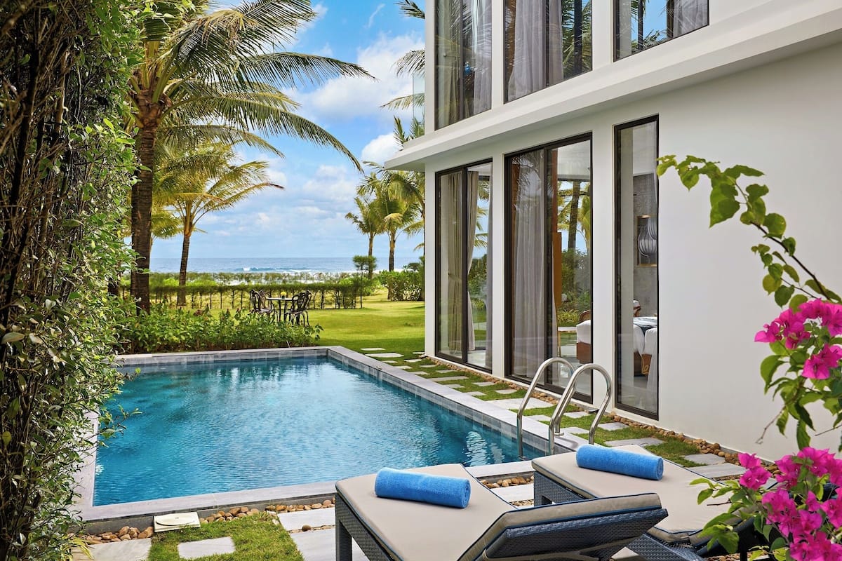 A modern pool area with a view of the ocean, a lounge chair, and a table with chairs.