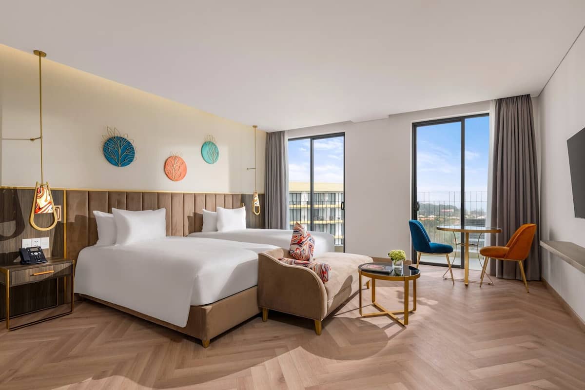 A modern hotel room with a large bed, a desk, a chair, and a balcony with a view.