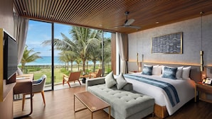 A modern hotel room with a large bed, a sofa, a desk, and a view of the ocean. - Royal Beachfront Resort & Spa Hoi An Danang (Da Nang)