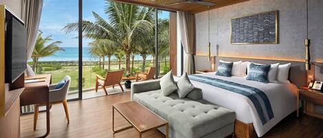 A modern hotel room with a large bed, a sofa, a desk, and a view of the ocean.