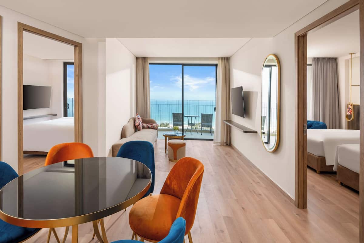 A hotel room with a balcony, a round dining table, and two sofas.