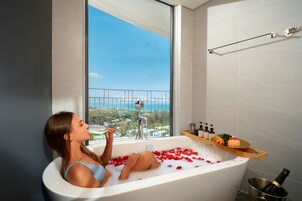 A woman in a bathtub with rose petals, a champagne bottle, and toiletries on a shelf.