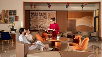 Un hall d’hôtel moderne, doté de canapés en cuir, d’un comptoir d’accueil en bois et d’un mur décoratif orné de divers objets suspendus.