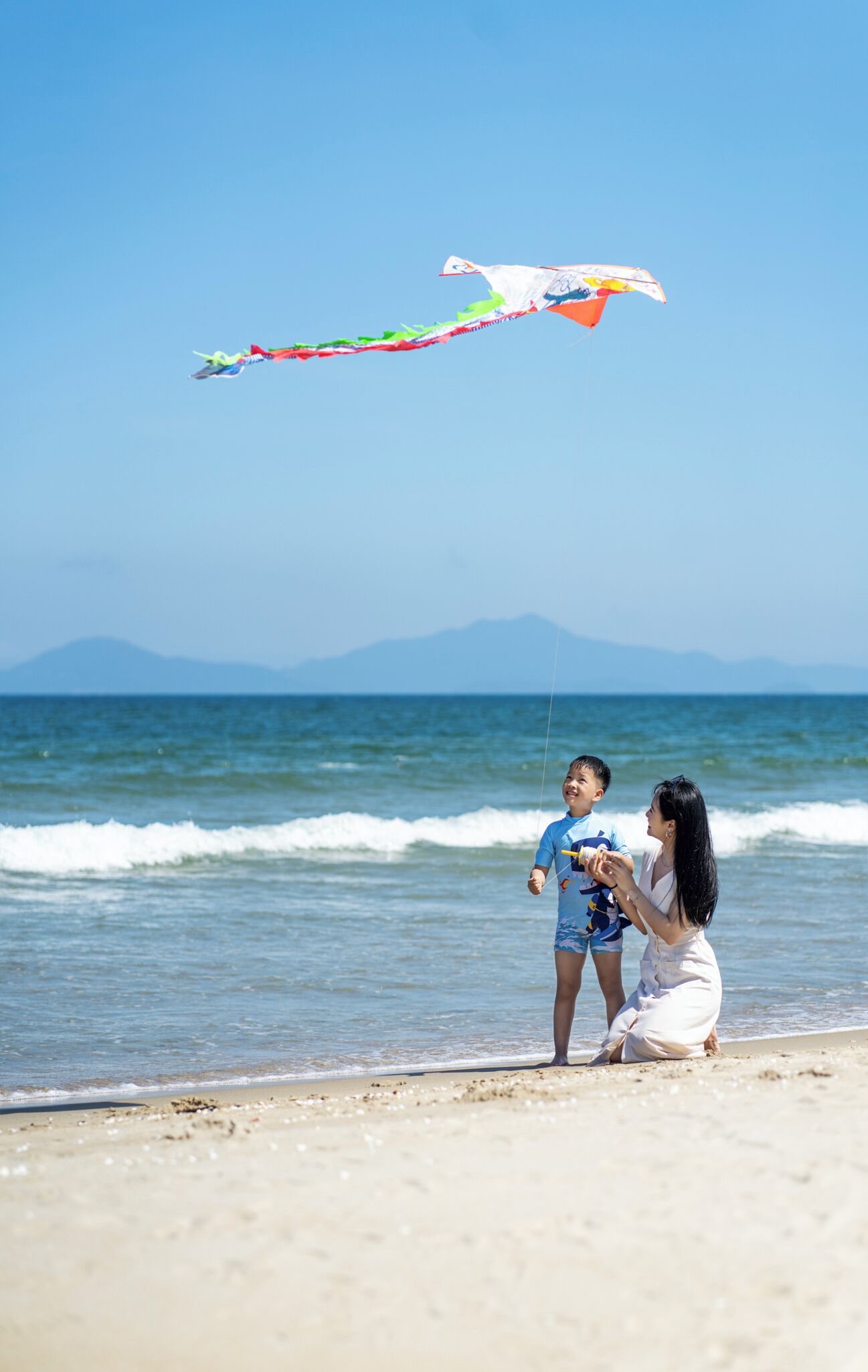 A beach scene with a person and a child flying a kite.
