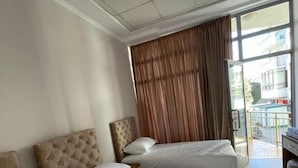 A hotel room with three beds, a large window with curtains, and a view of the outside. - Hotel Princ (Shkodër)