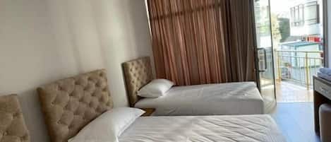 Habitación de hotel con tres camas, un ventanal con cortinas y vistas al exterior.