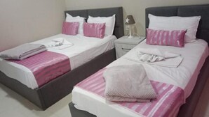 Two twin beds with pink and white bedding, a nightstand with a lamp, and a folded towel on each bed. - Hotel Princ (Shkodër)
