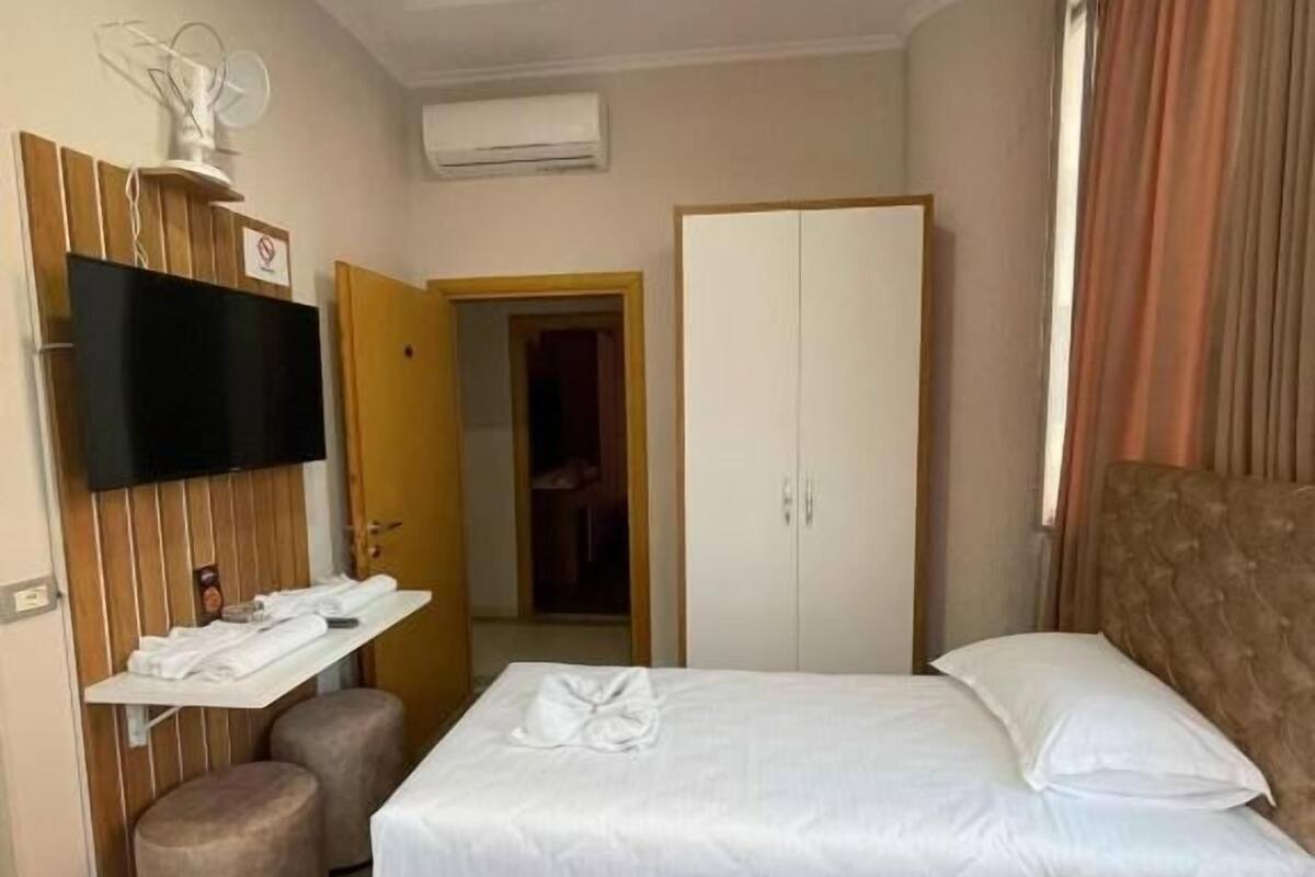 Quarto de hotel com duas camas, uma televisão presa a um painel de madeira, um guarda-roupa e uma pequena área de estar.