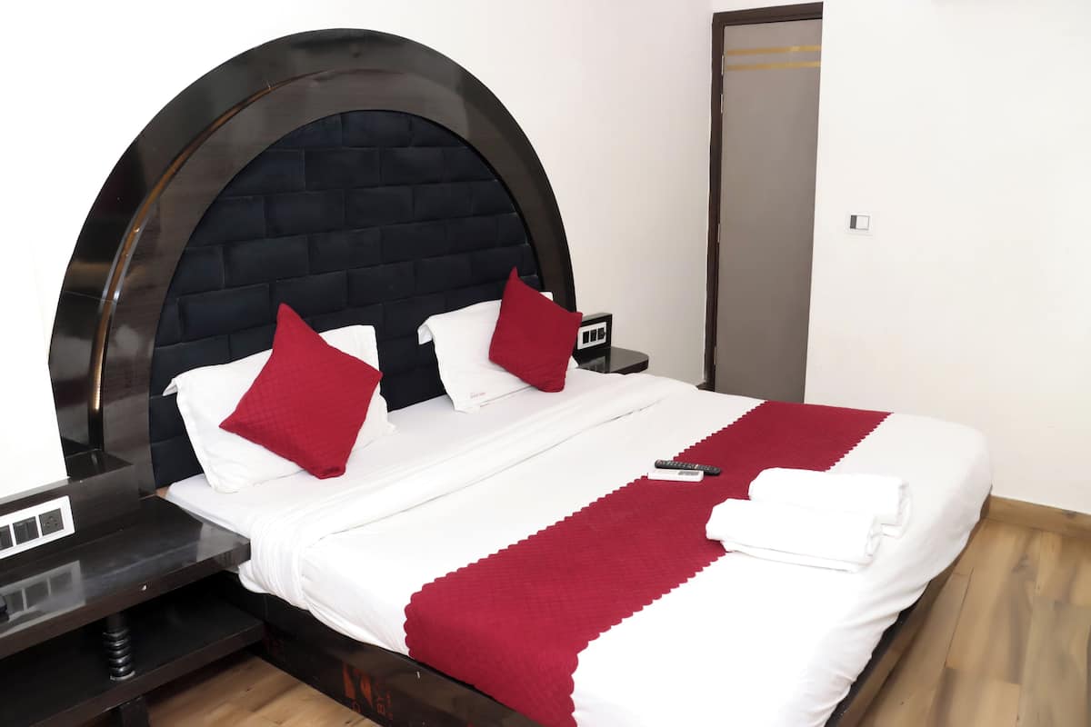 A bed with a black headboard, white bedding, red pillows, and a red throw blanket.
