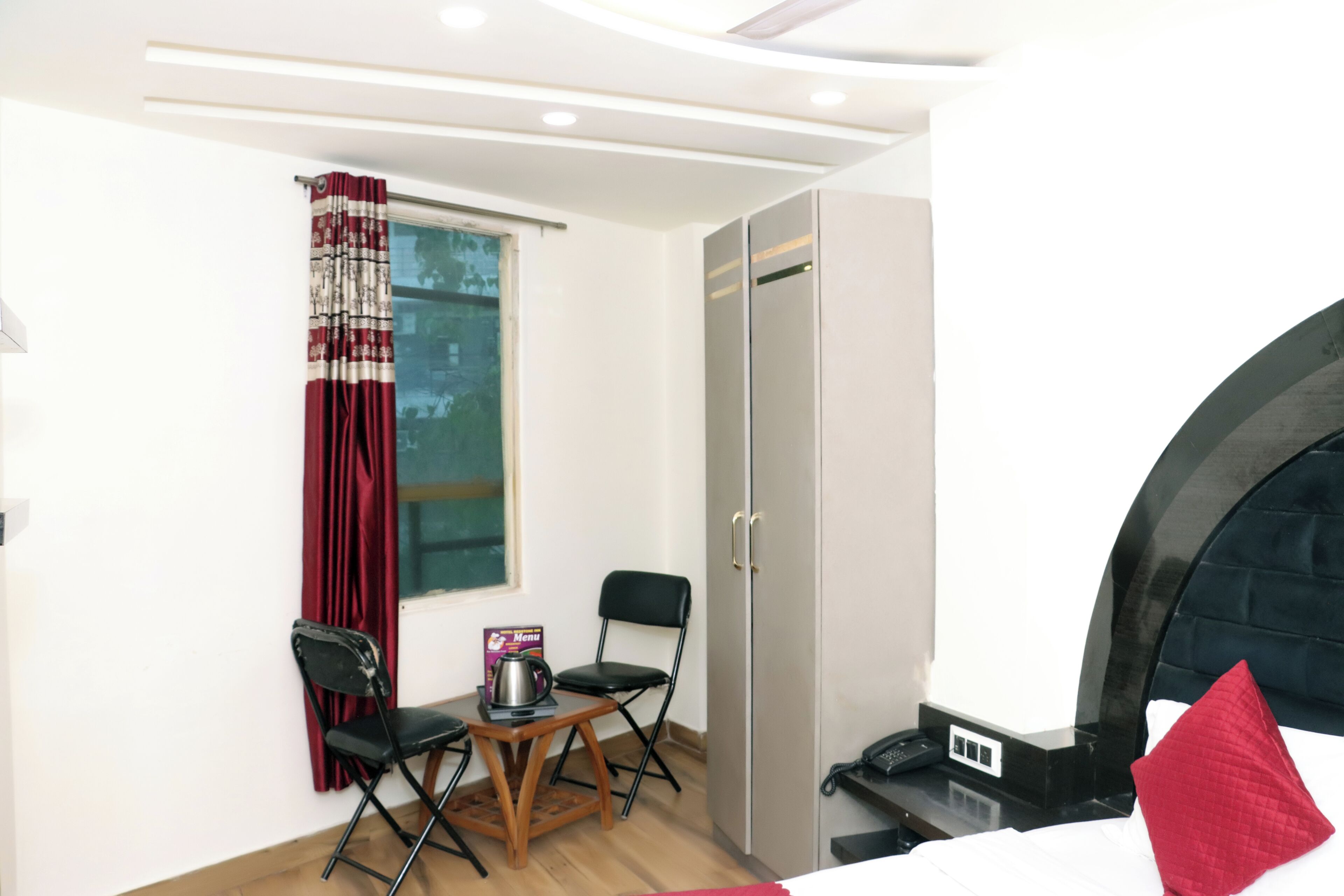 Habitación de hotel con cama, escritorio con hervidor, silla, armario y ventana con cortinas.