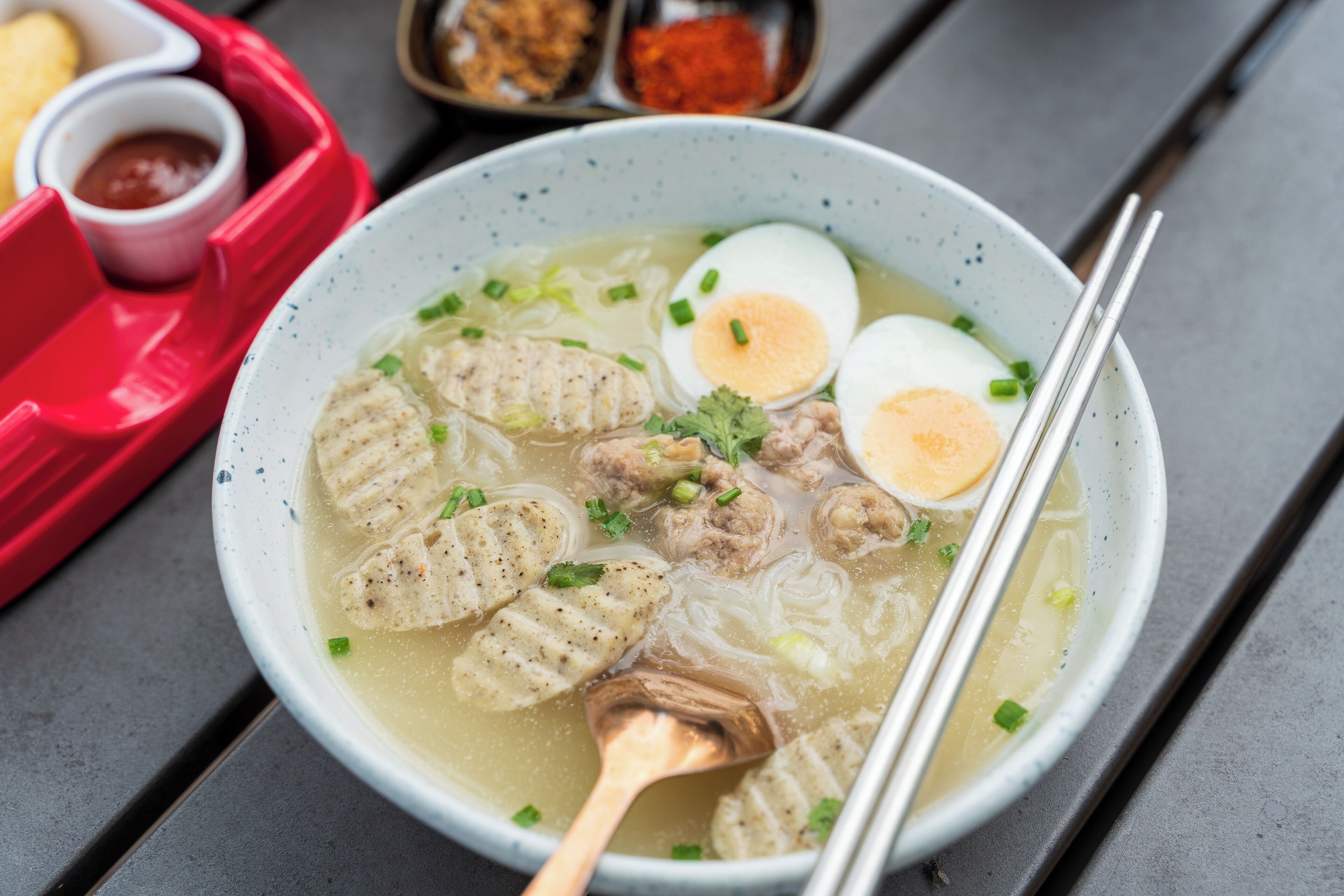 A bowl of soup with noodles, meatballs, and boiled eggs.