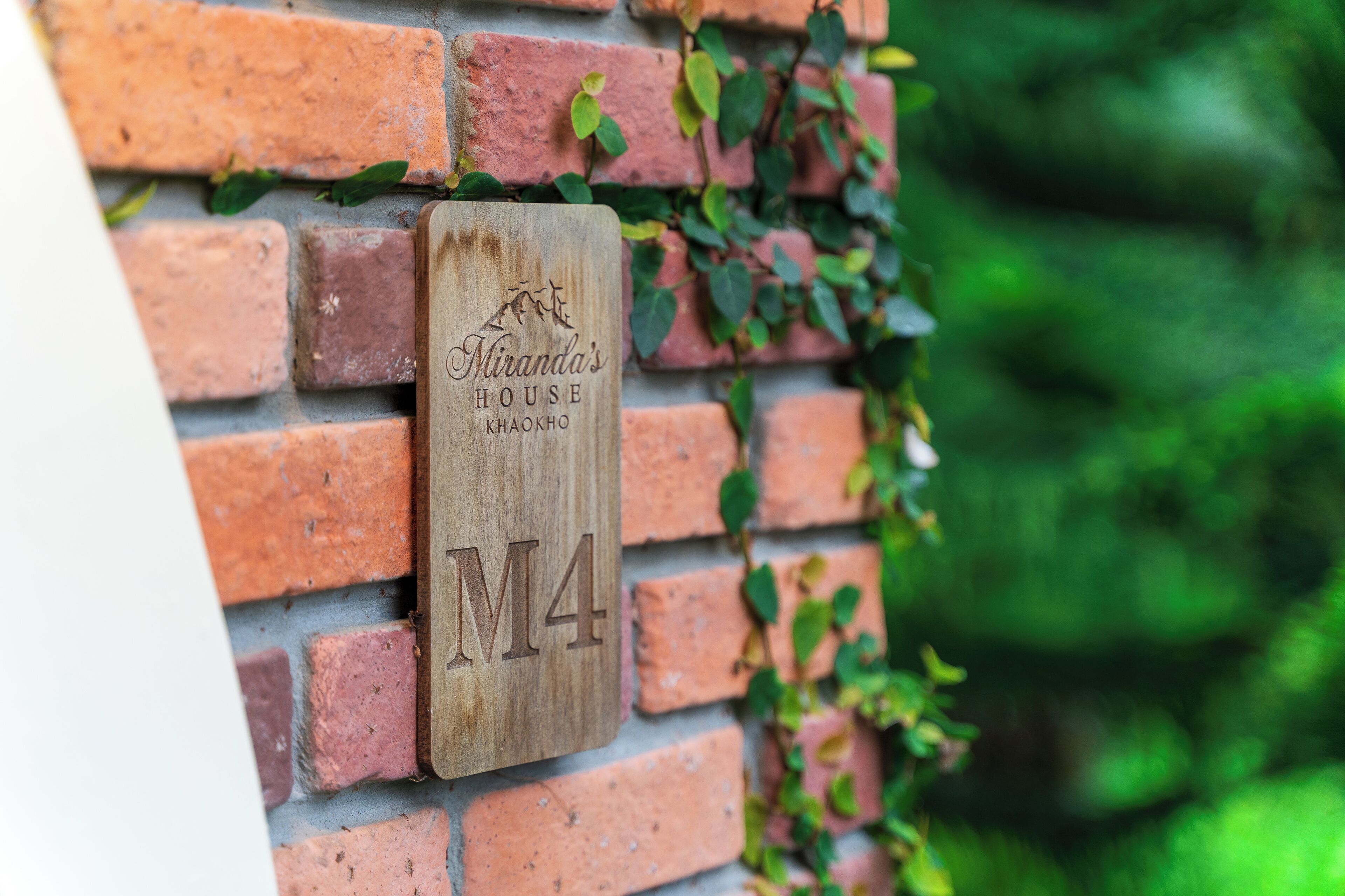 A wooden sign with the text "Iranda's House Khaokho M4" mounted on a brick wall.