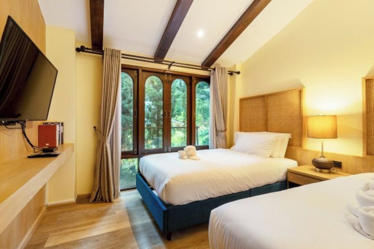 Habitación de hotel con dos camas, televisión, escritorio y un amplio ventanal con cortinas.