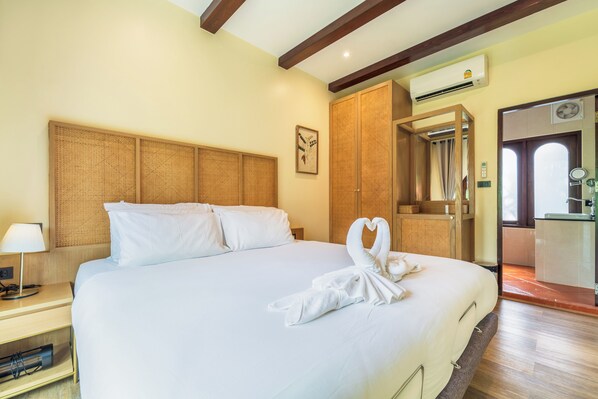 Habitación de hotel con una cama grande, una mesita de noche con lámpara, cabecero de madera, aire acondicionado instalado en la pared y puerta de baño visible a través de un vano abierto.