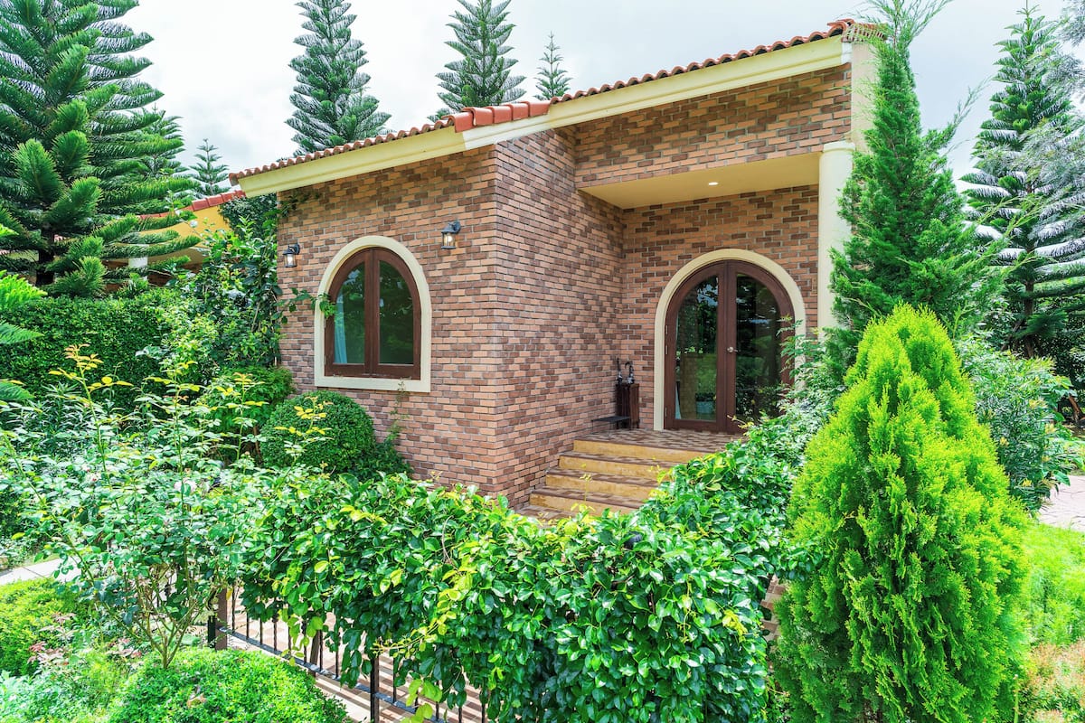 Una casa de dos plantas con fachada de ladrillo, dos ventanas arqueadas y tejado de tejas rojas.
