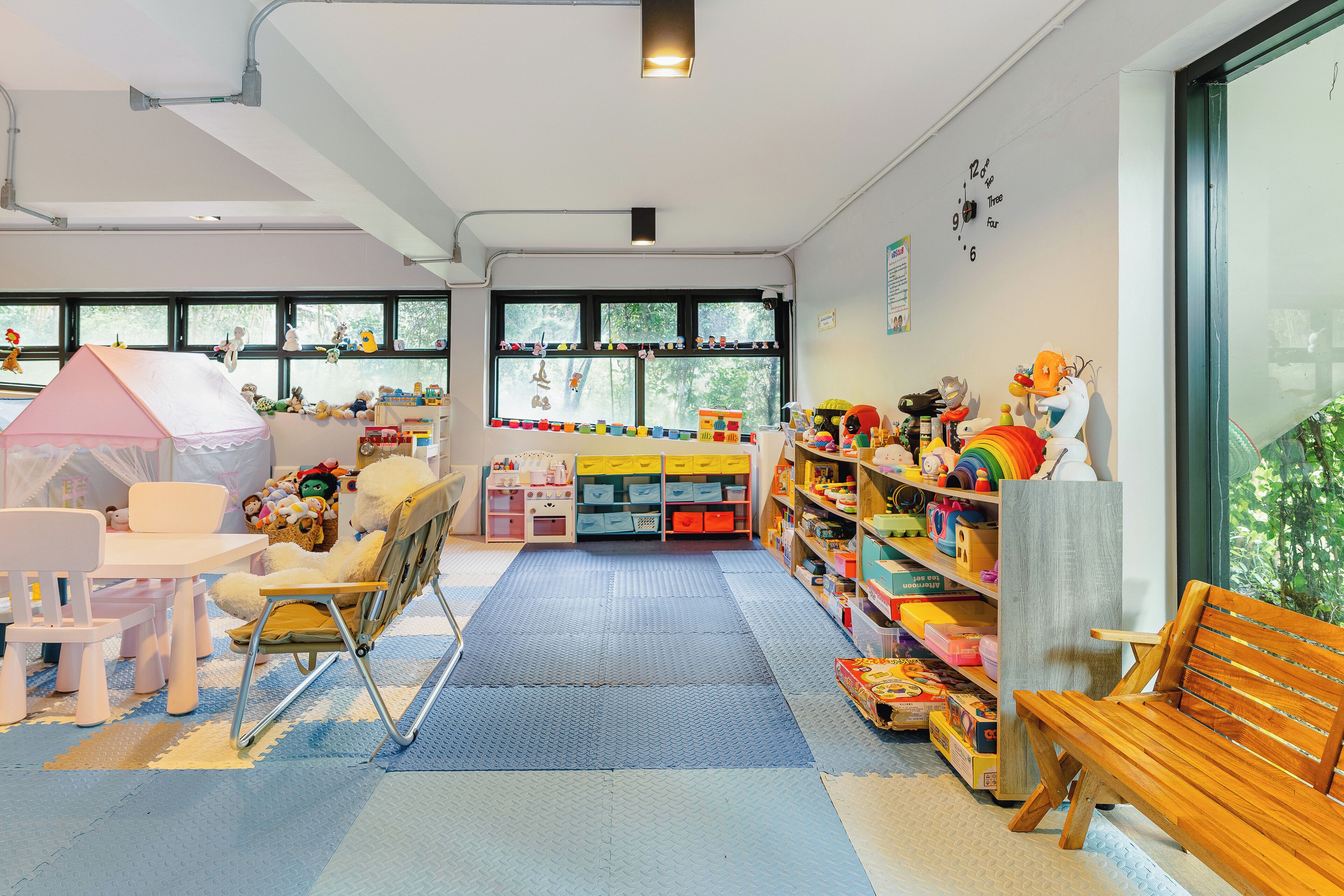 A child-friendly room with a play area, including a pink tent, a wooden bench, and a bookshelf filled with toys.