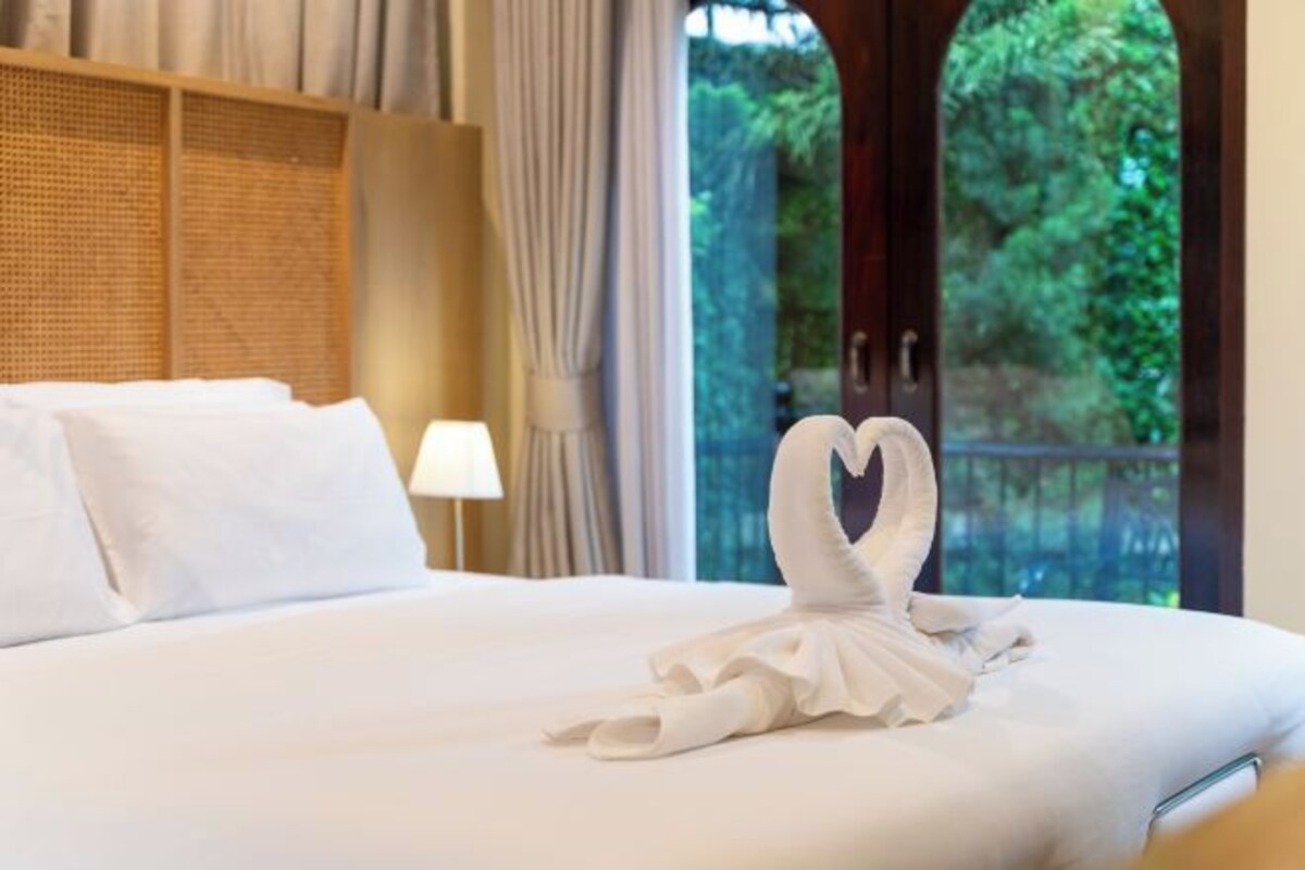 Una cama bien hecha con sábanas blancas y una disposición de toallas en forma de corazón sobre la cama.