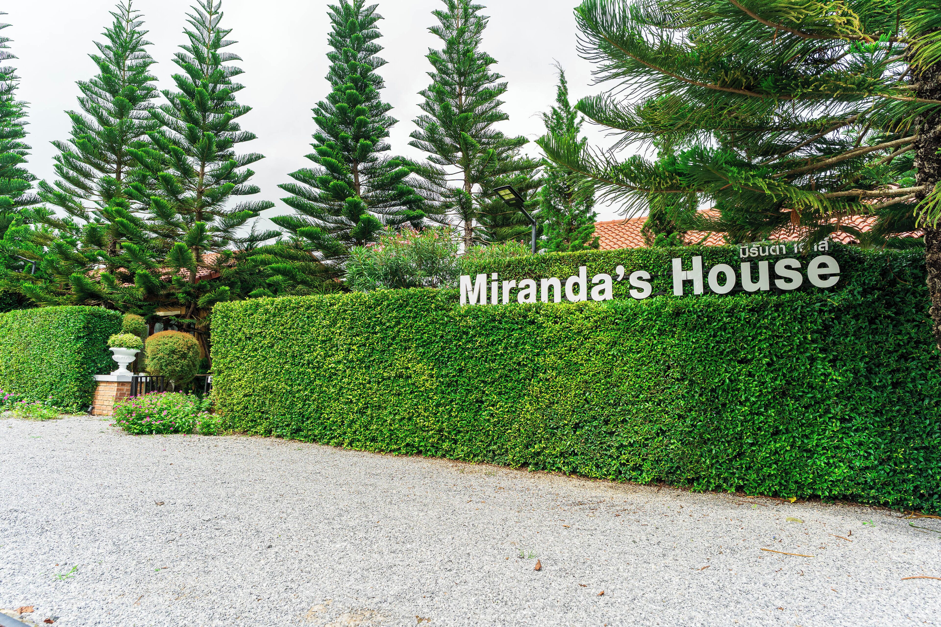 A well-maintained hedge with a sign reading "Miranda's House" in front of a building.