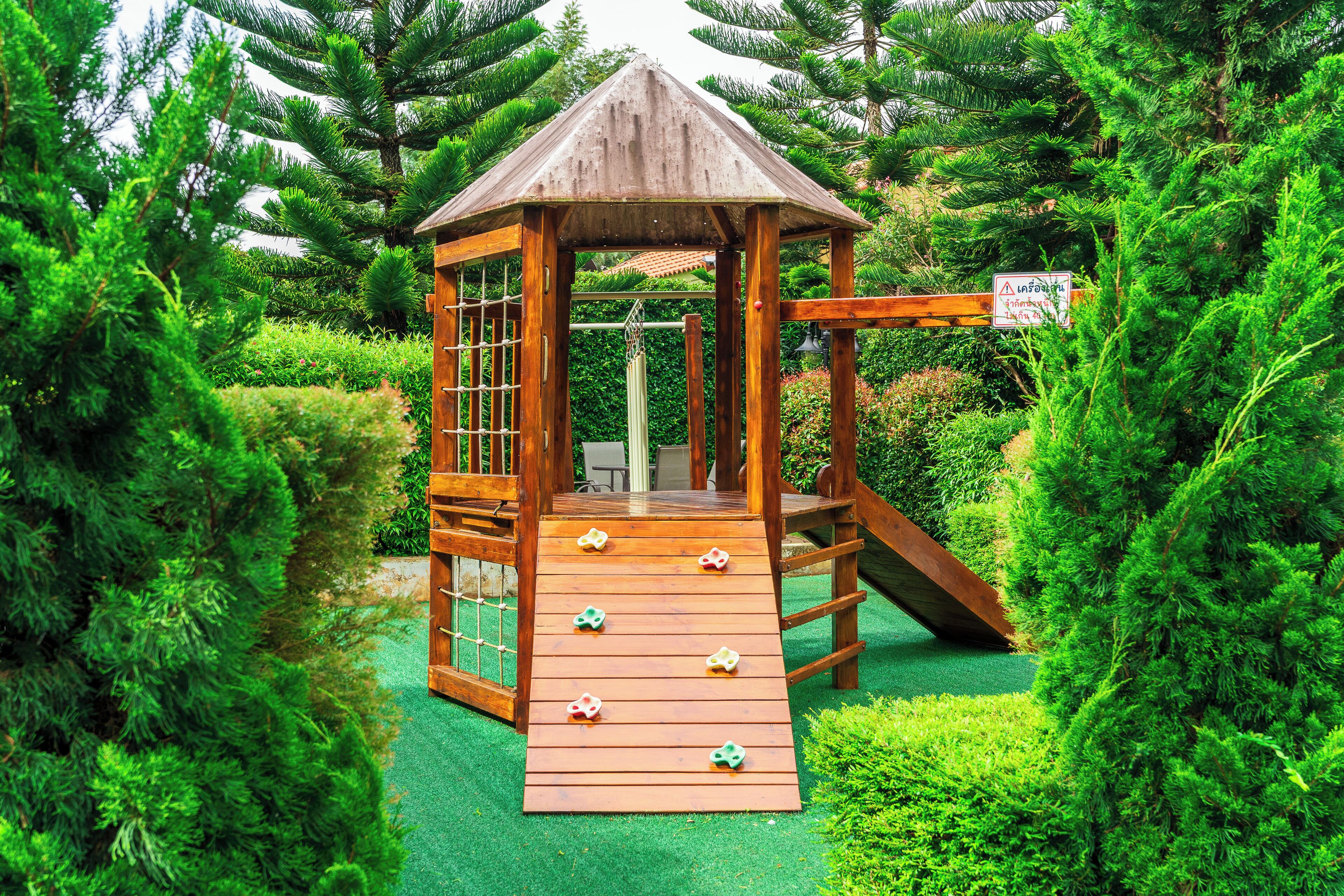 Une cabane en bois, dotée d’une rampe et d’un mur d’escalade, entourée d’une végétation luxuriante.