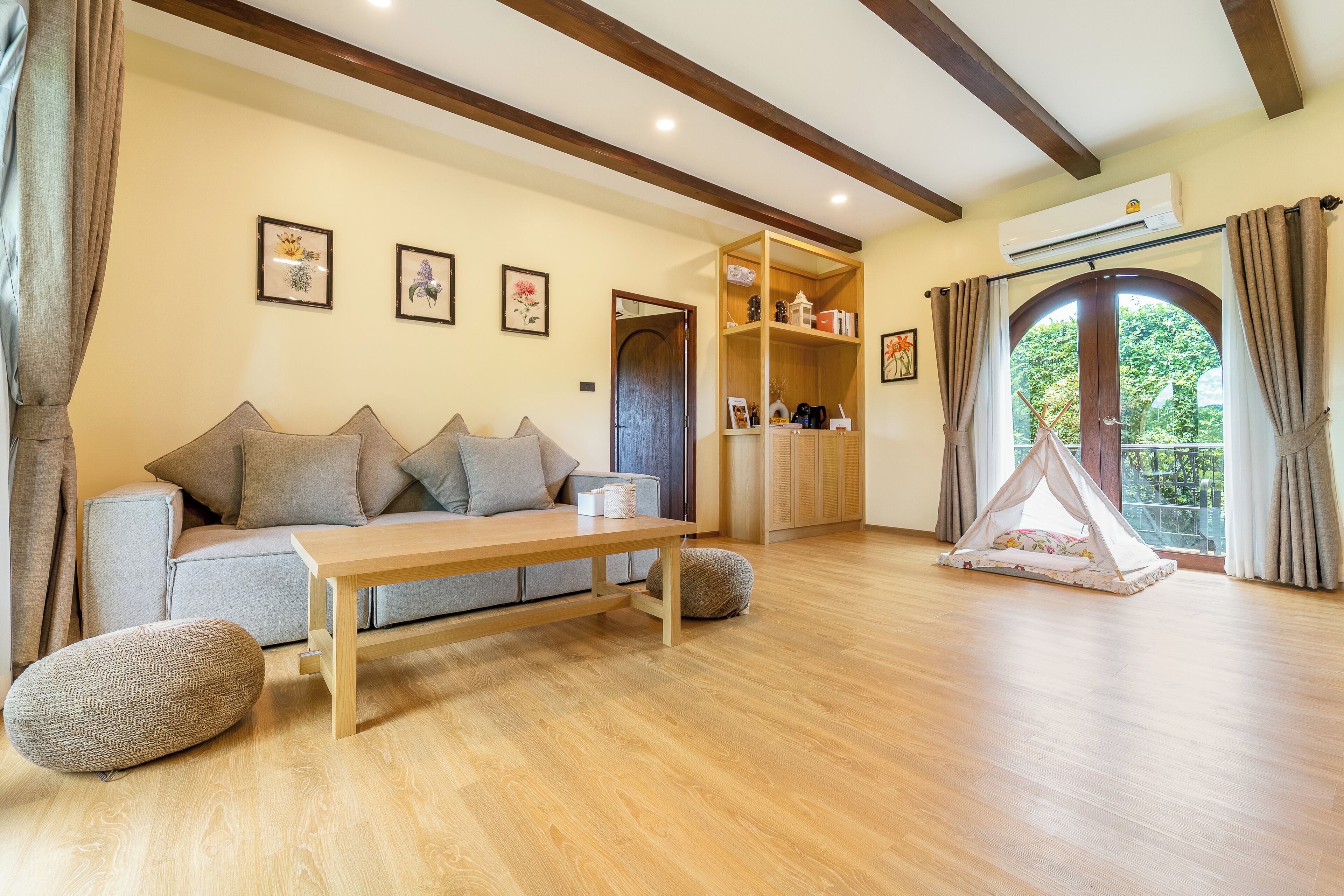 A living room with a sofa, a wooden coffee table, a small ottoman, a bookshelf, and a tent-like play area.