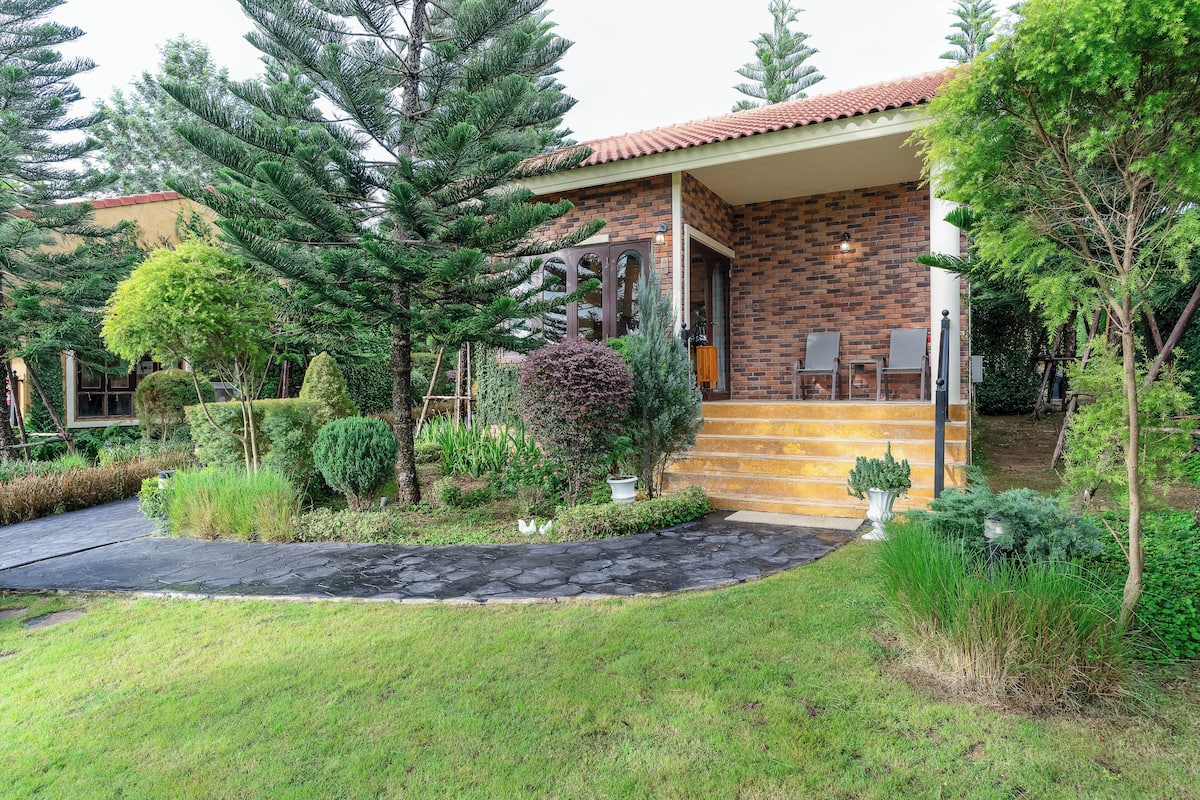 Una casa con fachada de ladrillo, un camino de piedra y un jardín bien cuidado con diversas plantas y árboles.
