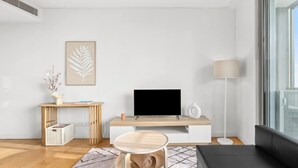 Una sala de estar moderna con un televisor de pantalla plana, una mesa de centro de madera, un sofá, una lámpara de pie y una obra de arte enmarcada en la pared.
