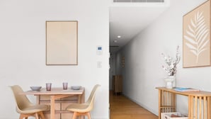Un comedor moderno con una mesa y sillas de madera, una obra de arte enmarcada en la pared y una mesita auxiliar con un jarrón.