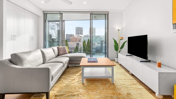 A modern living room with a sofa, a coffee table, a TV, and a large window with a city view. - Central Luminous 2 Beds With Balcony Aircon (Sydney)