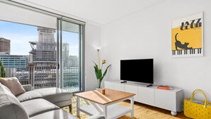 A modern living room with a sofa, a coffee table, a TV, and a yellow bag. - Central Luminous 2 Beds With Balcony Aircon (Sydney)