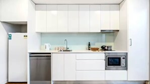 A modern kitchen with white cabinetry, a stainless steel dishwasher, a microwave, and a sink. - Central Art-deco 1bed With Balcony Aircon (Sydney)