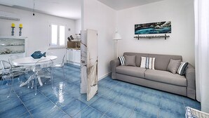 Uma sala de estar com sofá, uma mesa de jantar com cadeiras, uma área de cozinha e um quadro na parede.