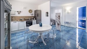 Cozinha moderna com armários brancos, uma mesa de jantar redonda e cadeiras transparentes.