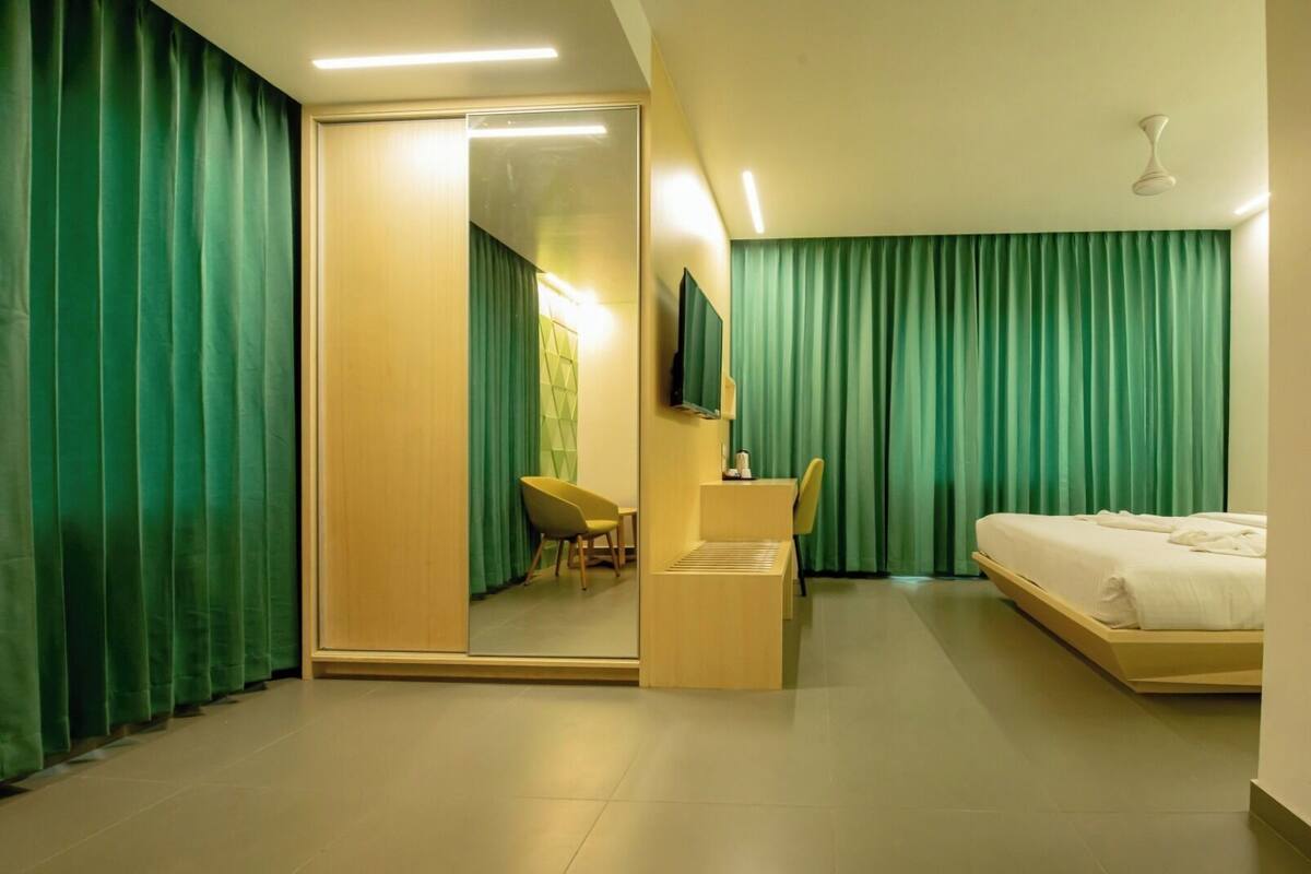 Habitació d'hotel amb un llit, escriptori amb una cadira, televisió i cortines verdes.