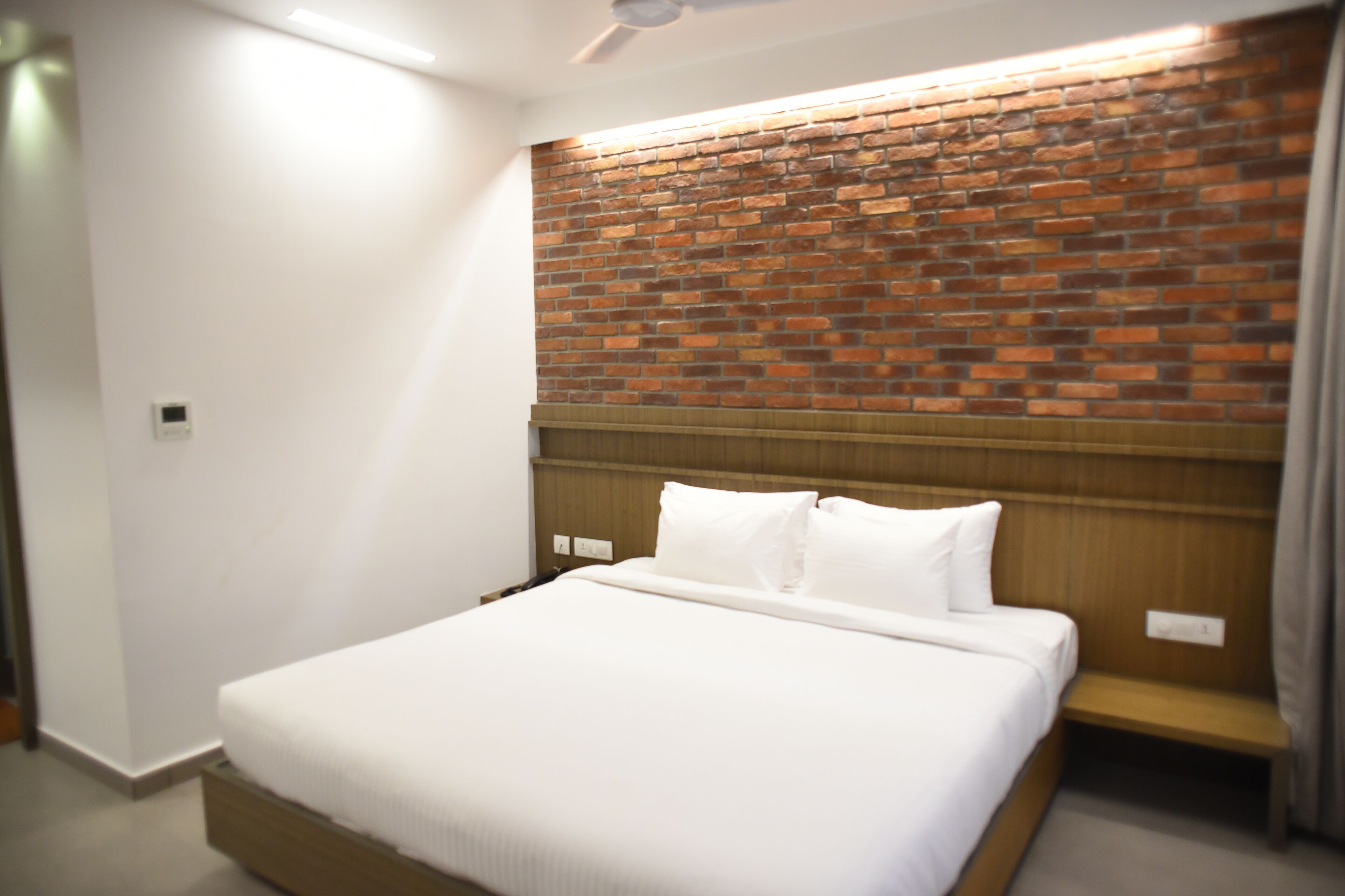 Una habitación de hotel con cabecera de ladrillo, una cama grande con ropa blanca y una mesita de noche de madera.